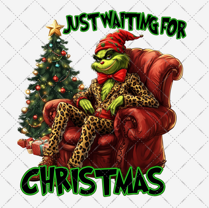 A green creature dressed in a leopard-print suit and a red Santa hat is seated on a red chair beside a Christmas tree adorned with decorations and surrounded by presents. The text above says "Just Waiting for Christmas." This high-resolution image, titled "Just Waiting for Christmas Transparent PNG File," is ideal for use as digital PNG files with a transparent background.